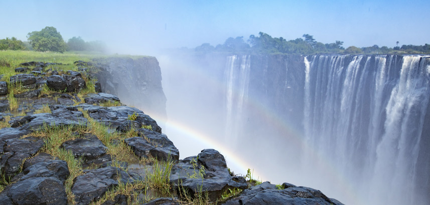 rainbows in the mist hand over the spray at the Victoria Falls gorge.