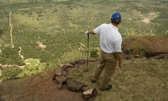 Golfer looking over the edge of the cliff at the extreme 19th hole with eh green below.