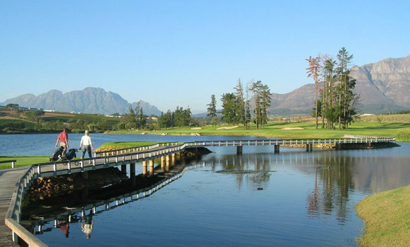 Golfers walking across the boardwalk over the lake at De Zalze golf club.