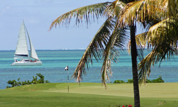 Golf green in Mauritius with passing catamaran boat.