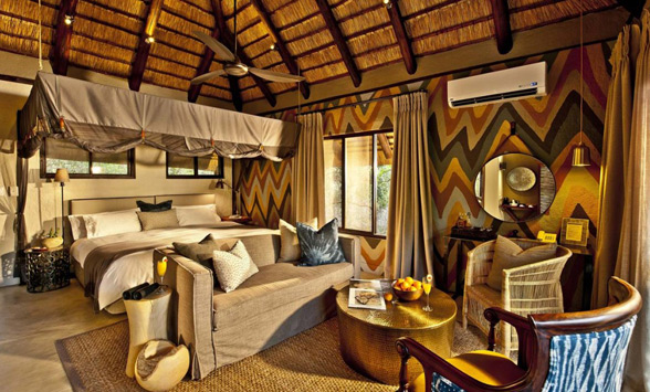 Colourful bedroom and lounge at safari lodge with thatched roof.