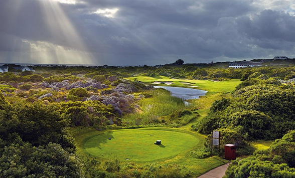 shafts of sunlight break through the grey clouds over the fairway of a golf course.