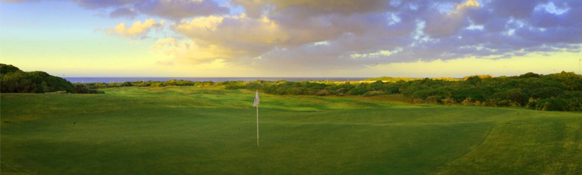 Dark clouds over the golf course green and ocean in the distance.