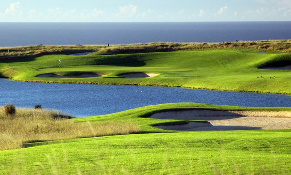 Green grass fairways on either side of the lake with bunkers surrounding the greens.