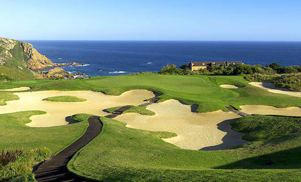 dramatic views of the indian ocean with large cavernous bunkers surrounding a golf course green.
