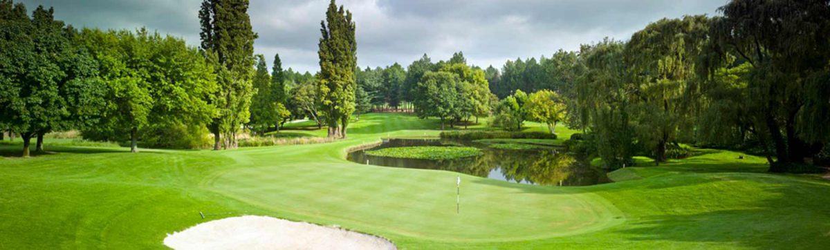 wide angle view of the golf course with bunkers, a small lake and tall trees surrounding the fairway.