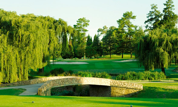 long shadows on the fairway as golfers start their round with a tee shot over the stone bridge to the fairway beyond.