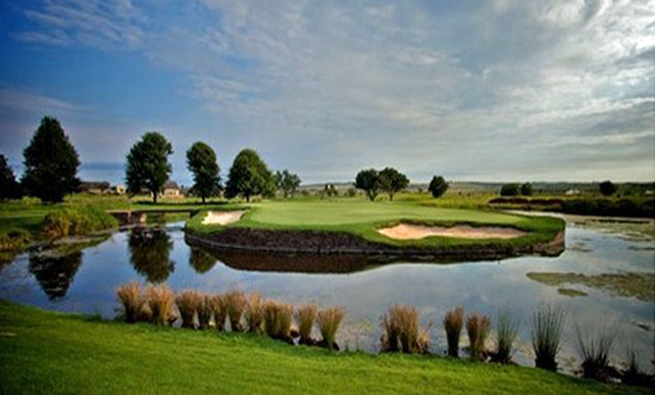 A mackerel sky with light clouds are reflected in the water around the island green on the golf course.