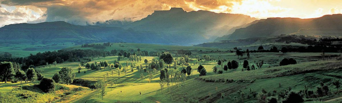 Evening sun casts long shadows across the fairways, silhouetting the mountains in the distance.