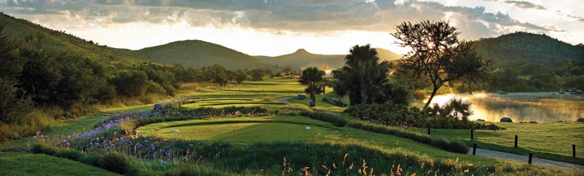 sunrise over the hills is reflected in the lake to the right of the empty tee boxes on the golf course.