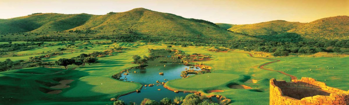 long shadows fall across the fairways and lake at the golf course with an orange hue to the surrounding sky.