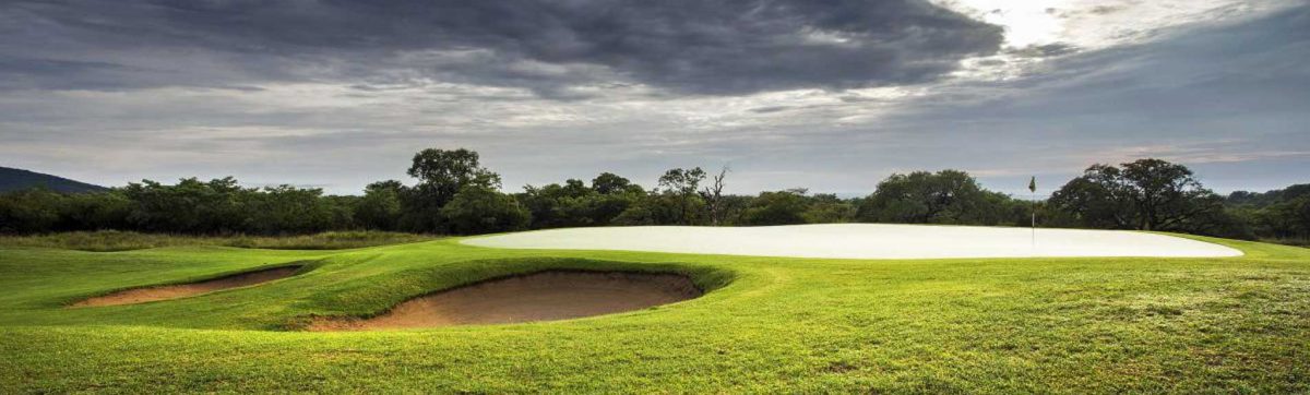 panoramic view of a golf green with flag and sandy bunkers guarding the left edge.