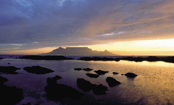 Sihouette of Table Mountain in the distance and rocks in the foreground with a yellow sky selected in the water.