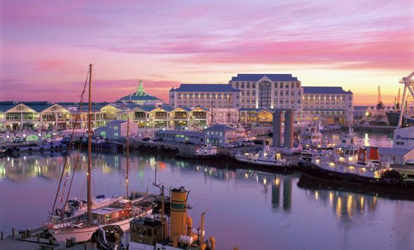 Pink sky reflected in the water of the harbour in Cape Town with lights and boats.