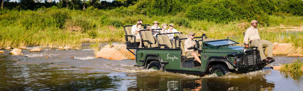 Family on a game drive vehicle as it ploughs through the Sand river.