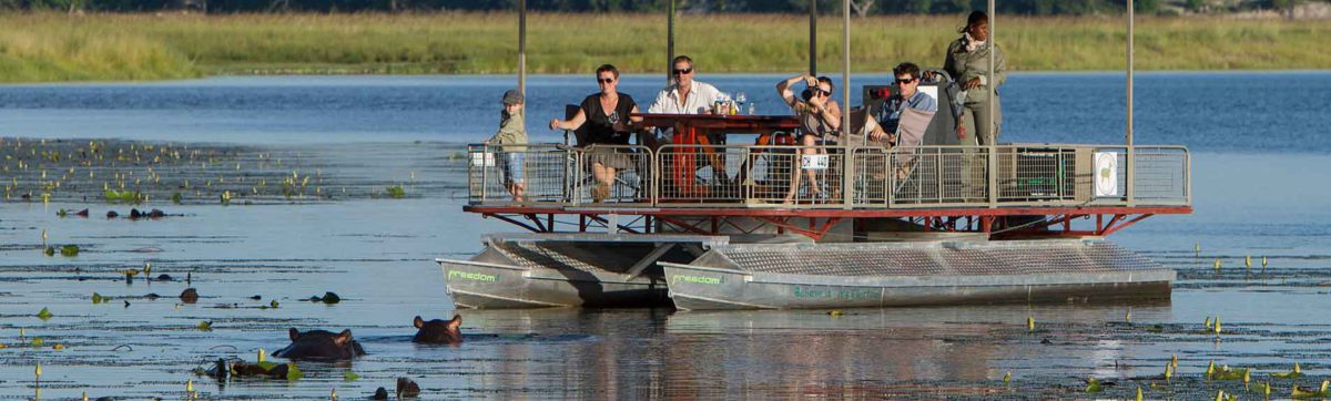 Tourist family watching hippos from a safari cruise on the Chobe river.