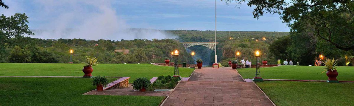 dusk sets over the lawn at the Victoria Falls Hotel with views of the spray from the falls hangs in the air.