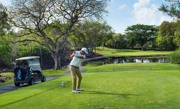 Golfer teeing off across the lake at Belle Mare Plage.