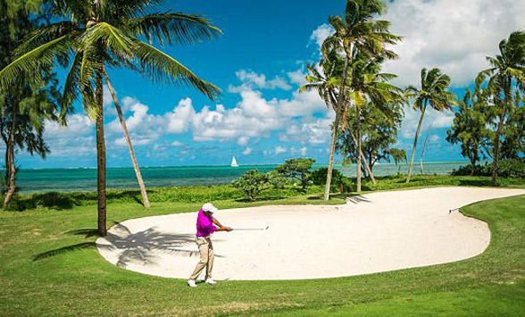 Golfer on the fairway at Anahita surrounded by palms and a turquoise blue lagoon.