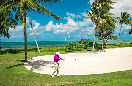 golfer playing his shot from the bunker on a palm fringed golf course in Mauritius.