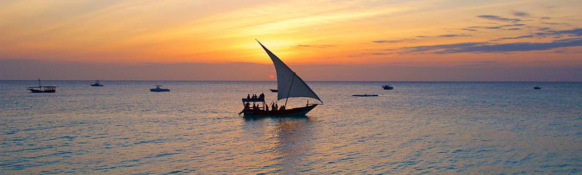 dhow boat sailing on the ocean near Stone Town, Zanzibar as the sun sets.