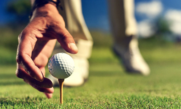 golfer placing a golf ball on the tee.