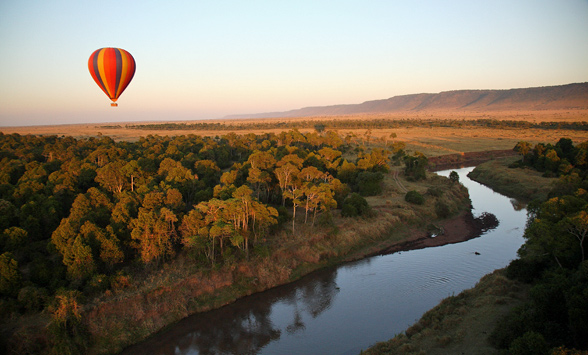 Hot air balloon travelling over a river in the masia mara